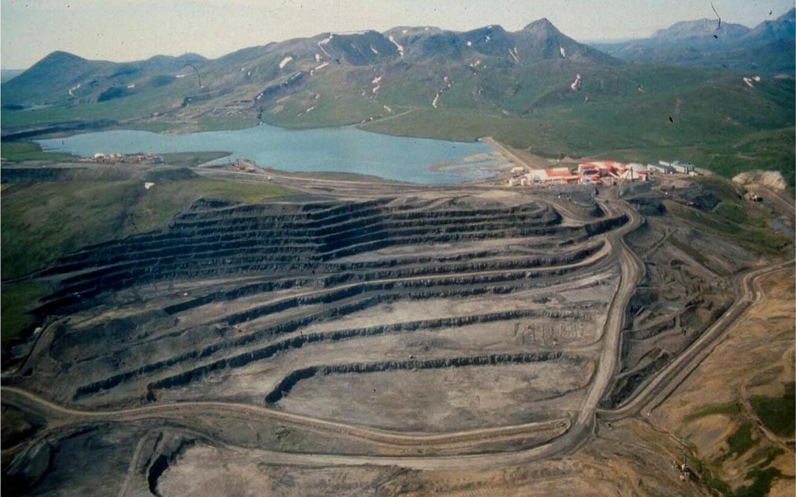 Aerial view of a terraced open-pit zinc mine beside a lake and mountains