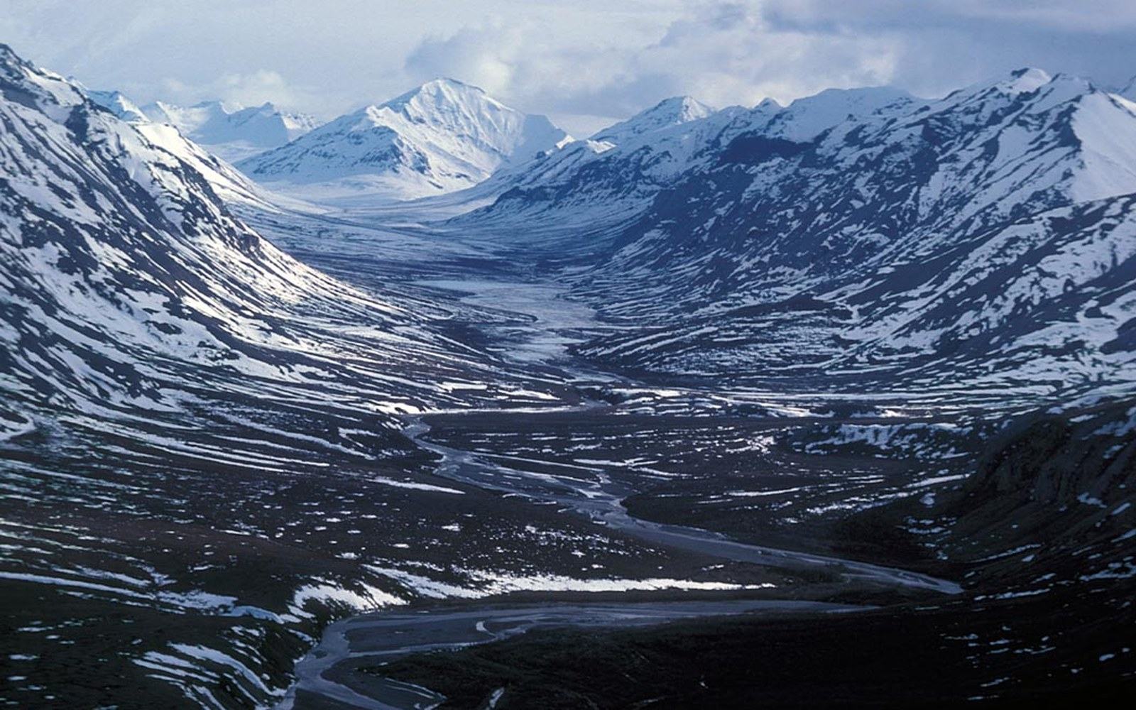 A braided river winds through a snow-covered valley in the Brooks Range mountains